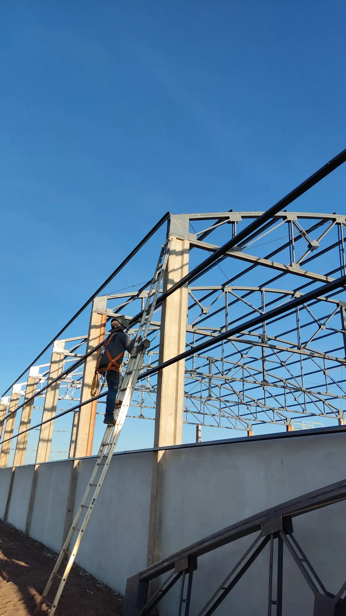 Montador fixando treliça metálica em coluna de concreto durante obra de galpão — MR Serralheria